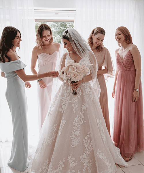 Braut im Hochzeitskleid wird von Brautjungfern und Freundinnen beim Ankleiden unterstützt