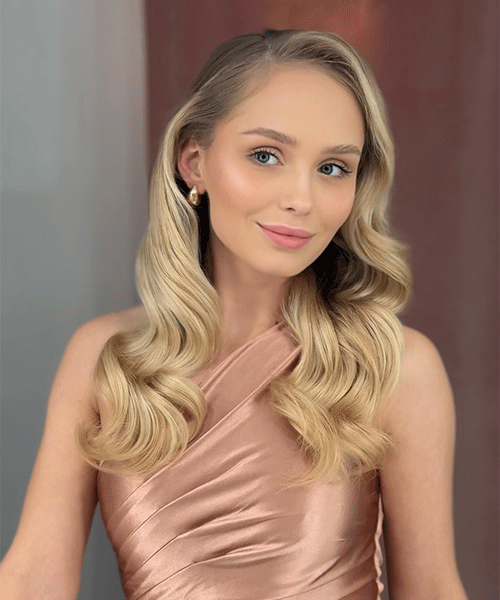 Junge Frau mit langen blonden Haaren und elegantem Make-up posiert im rosafarbenen Satin-Oberteil